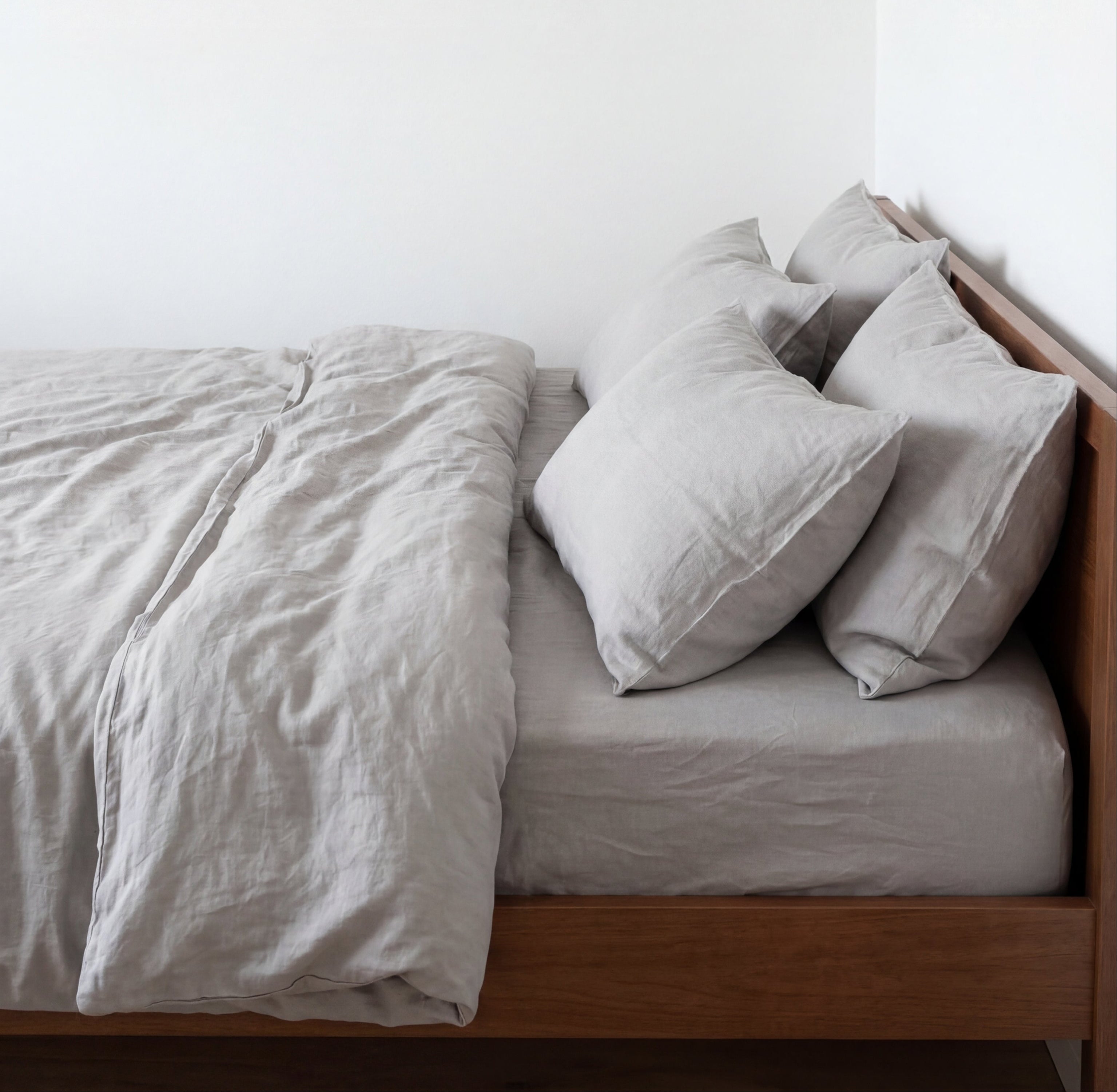 Minimal bedroom with a wooden bed dressed in soft neutral linen bedding and pillows.