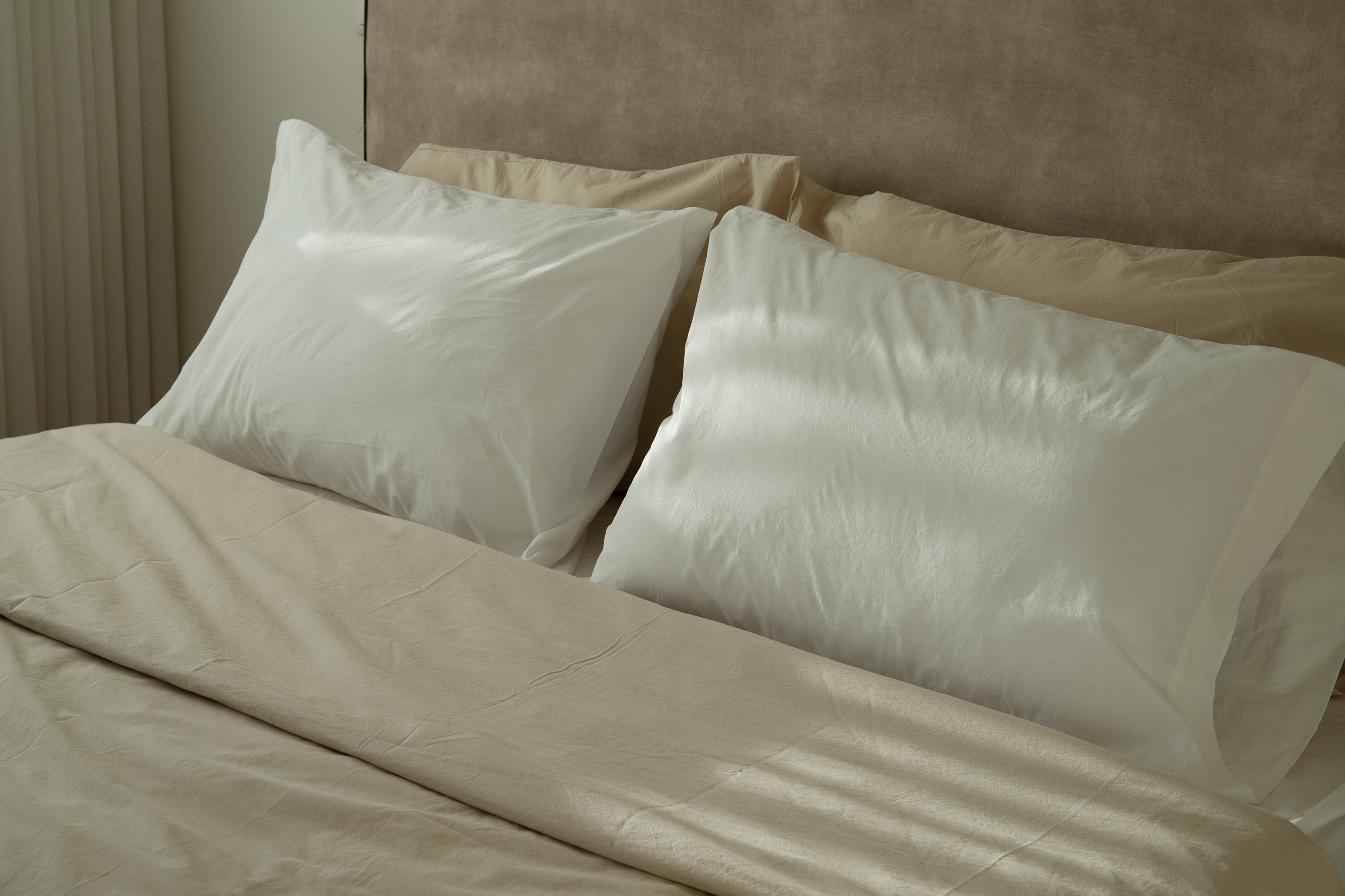 Bed with soft cotton bedding in neutral tones and white pillowcases in natural light.
