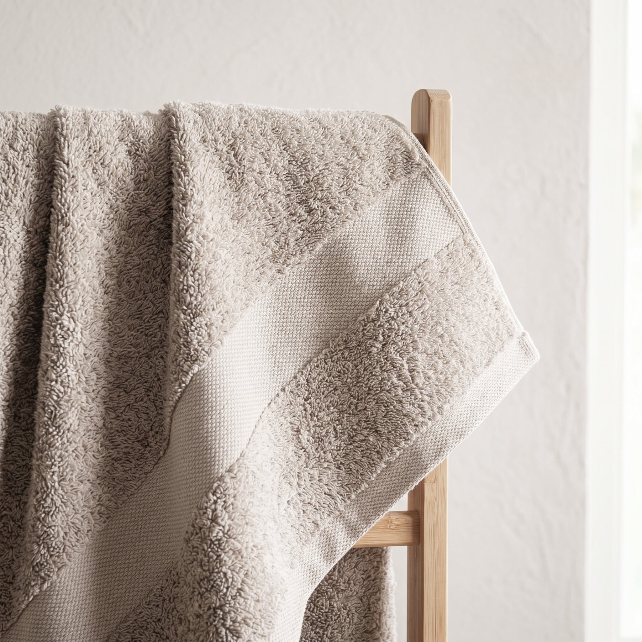 Relaxed cotton towel draped over a wooden rail with visible texture and soft natural light.