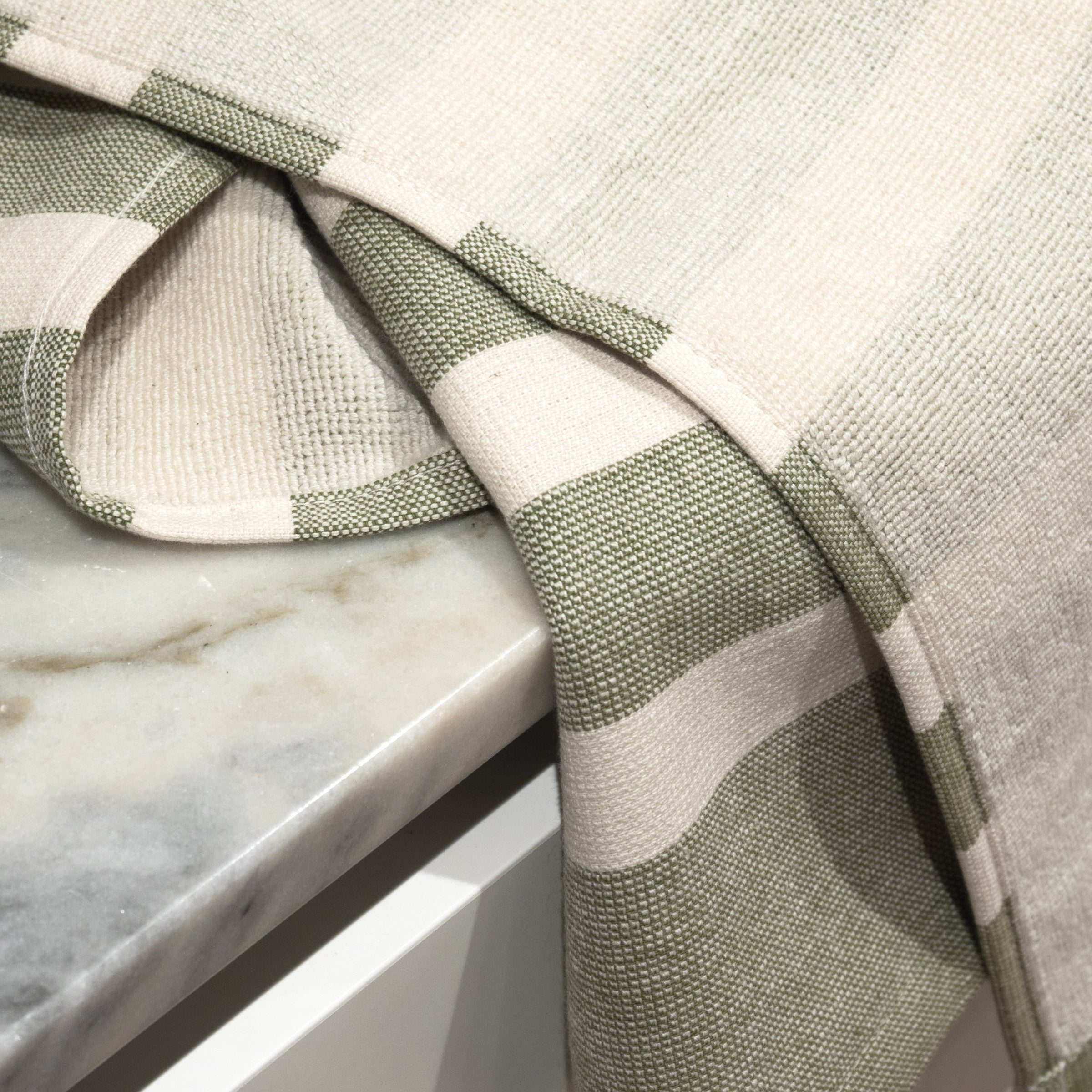 Cotton kitchen towel with green stripes and terry backing placed on a marble surface.