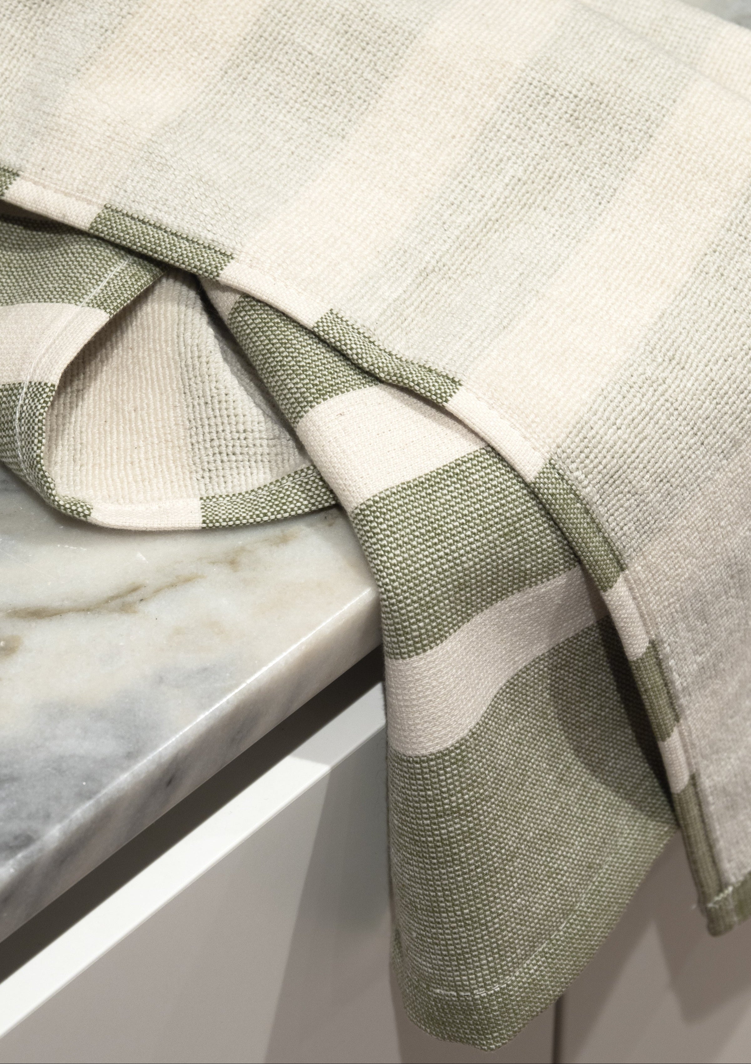 Cotton kitchen towel with green stripes and terry backing placed on a marble surface.