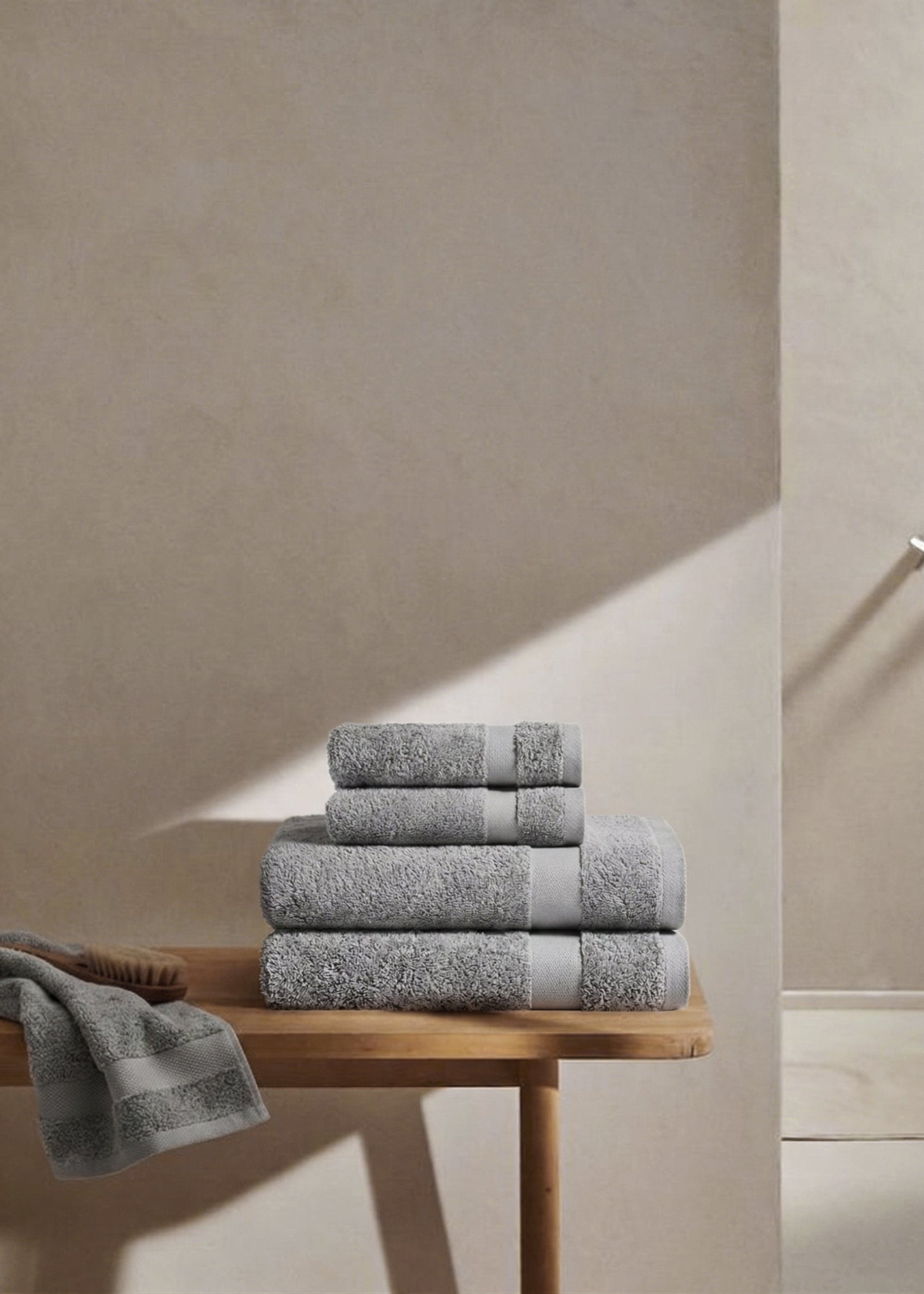 Folded cotton towels in soft grey tones placed on a wooden bench in natural light.