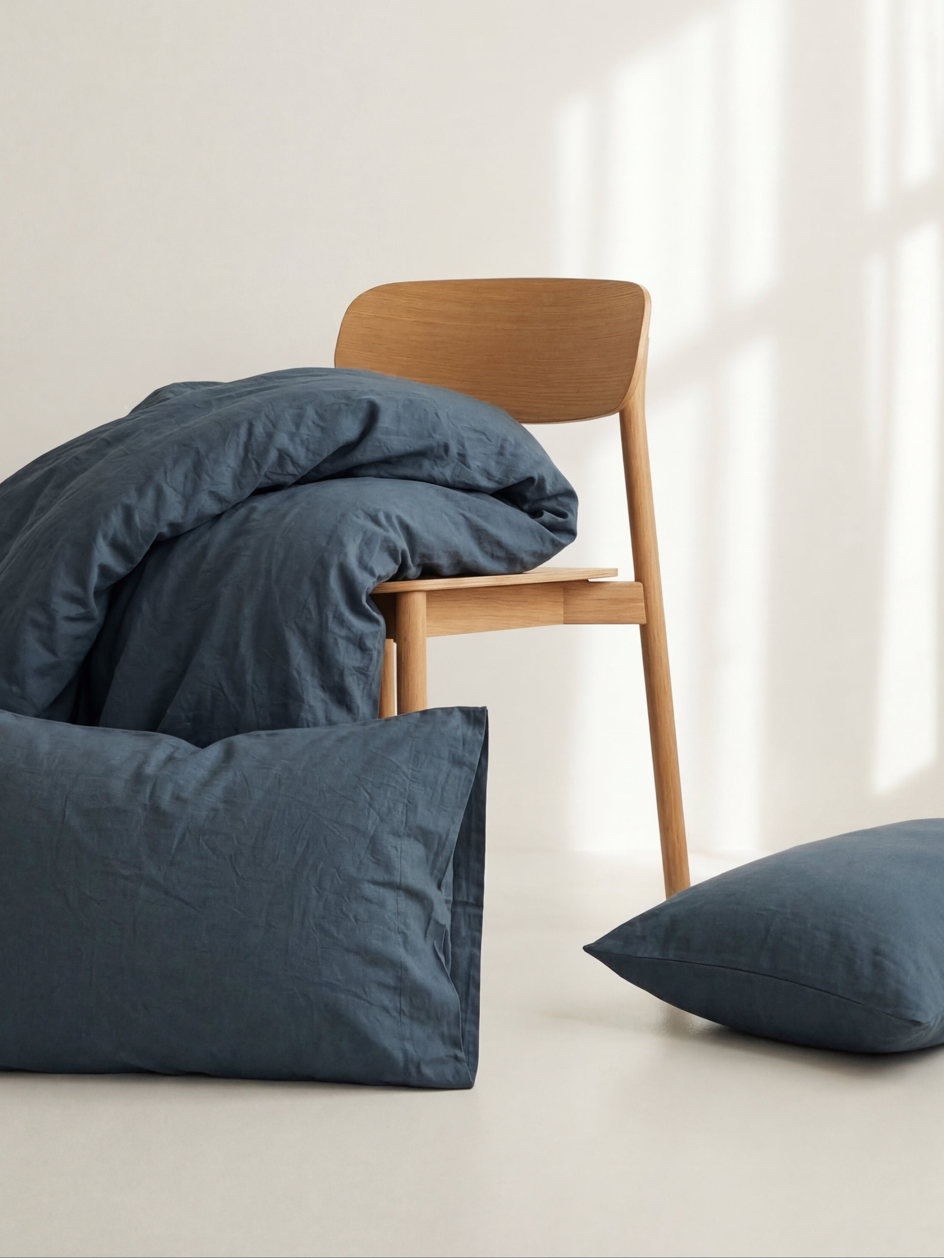 Soft cotton bedding in deep blue tones styled on a wooden chair in natural light.