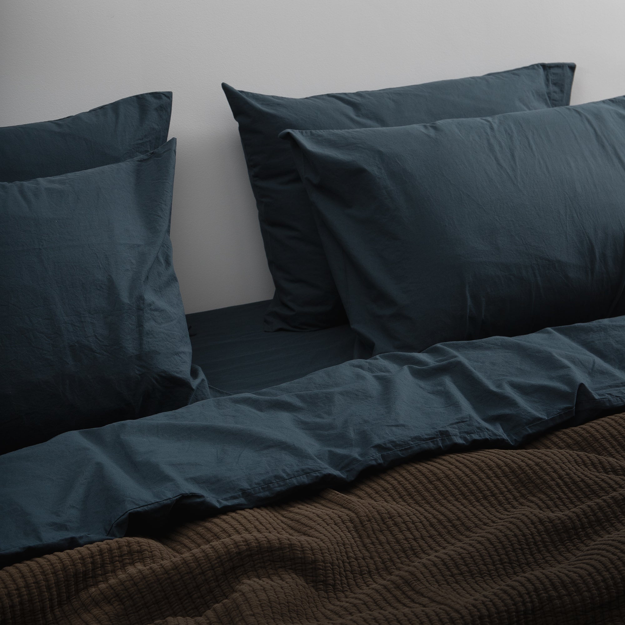 Bed with soft cotton bedding in deep blue tones styled in a calm, minimal setting.