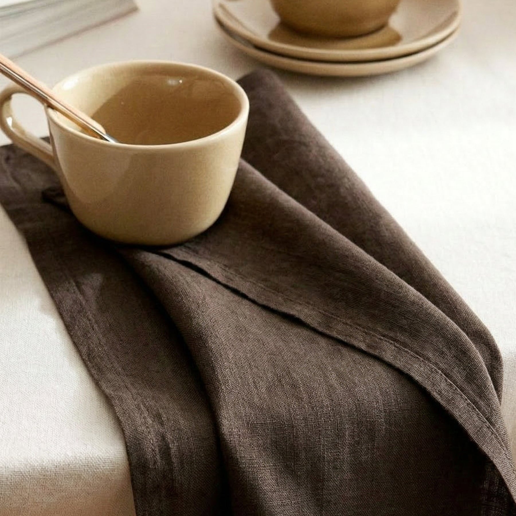 Linen napkin in deep brown tone styled on a table with ceramic cups.