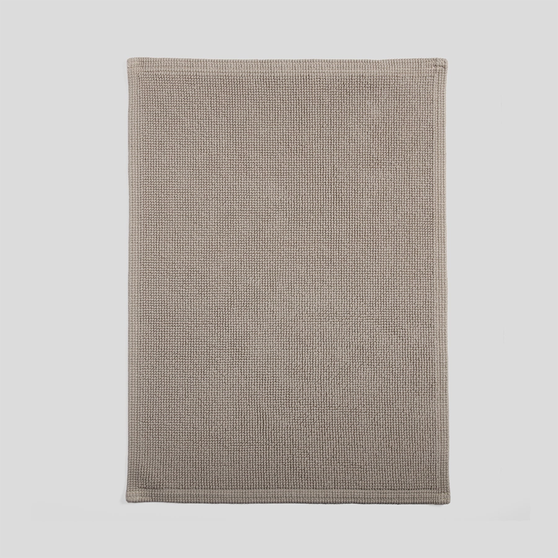 Cotton bath mat in sand with a dense woven texture and clean edges.