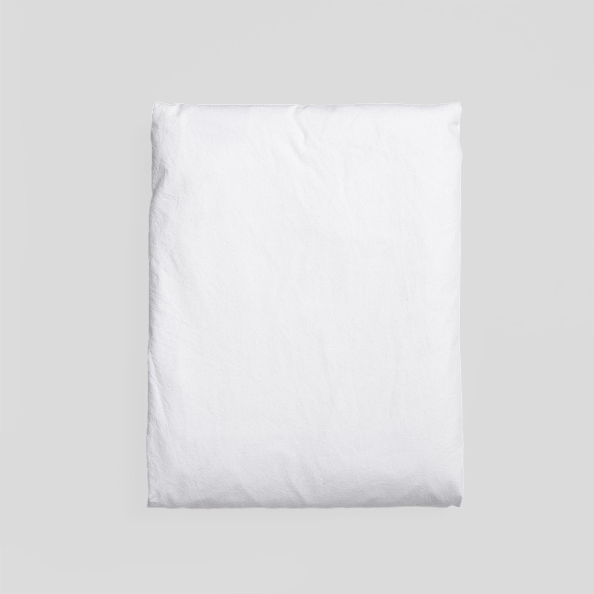 Pure white organic cotton fitted sheet folded, ideal for fresh and minimalist bedroom style.
