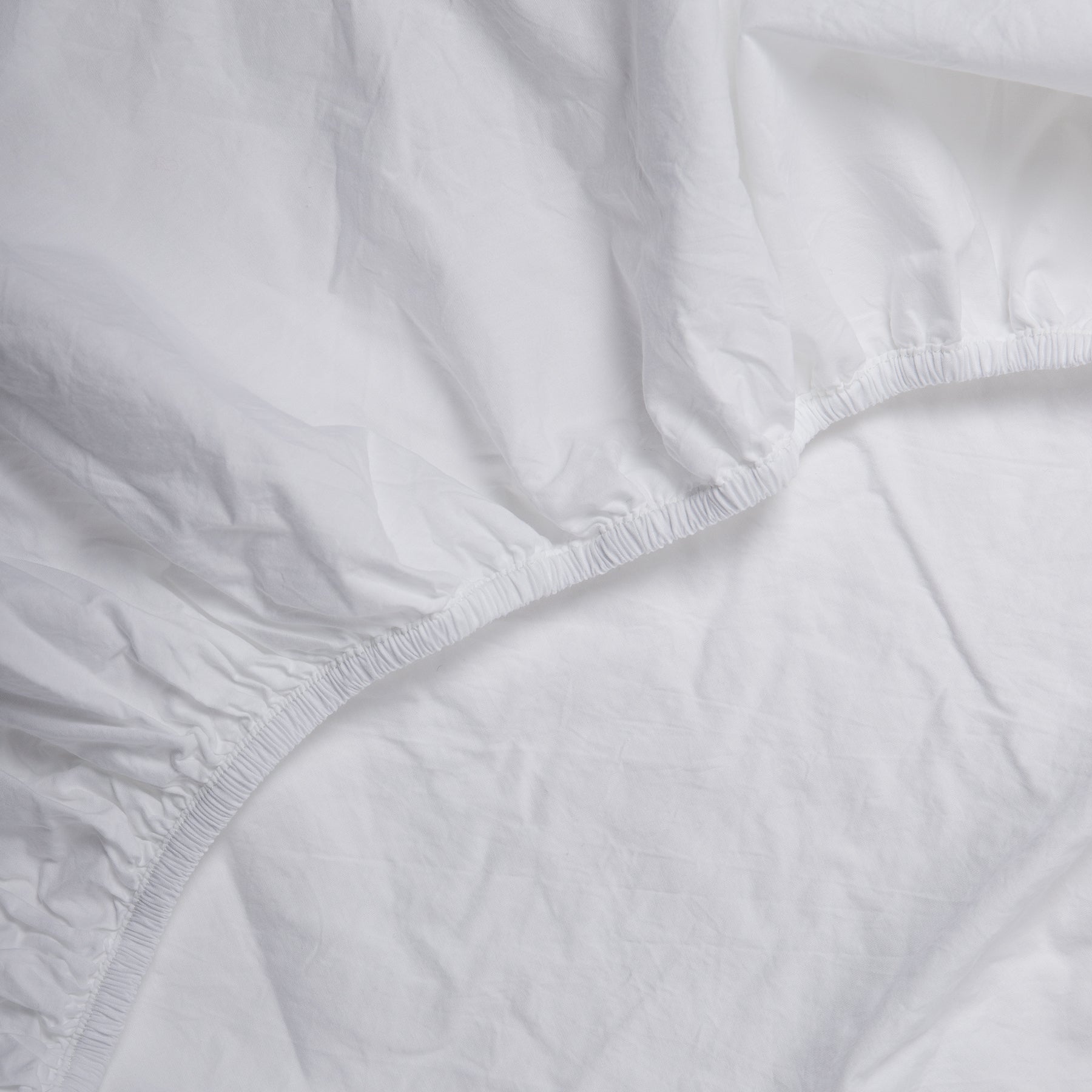 Detail of elastic edge on pure white fitted sheet made from soft certified organic cotton.