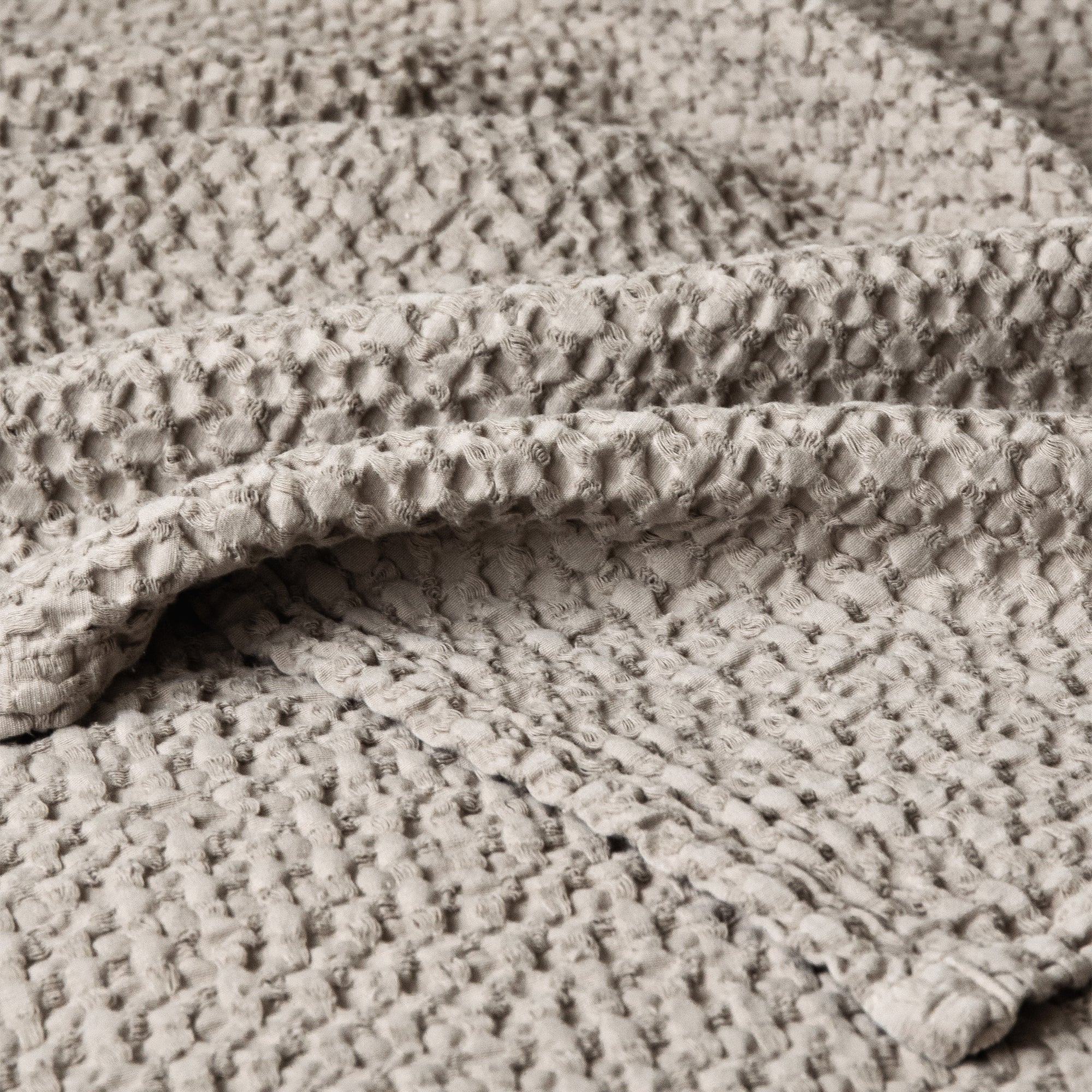 Close-up of a textured bedspread with a soft woven pattern and layered folds.