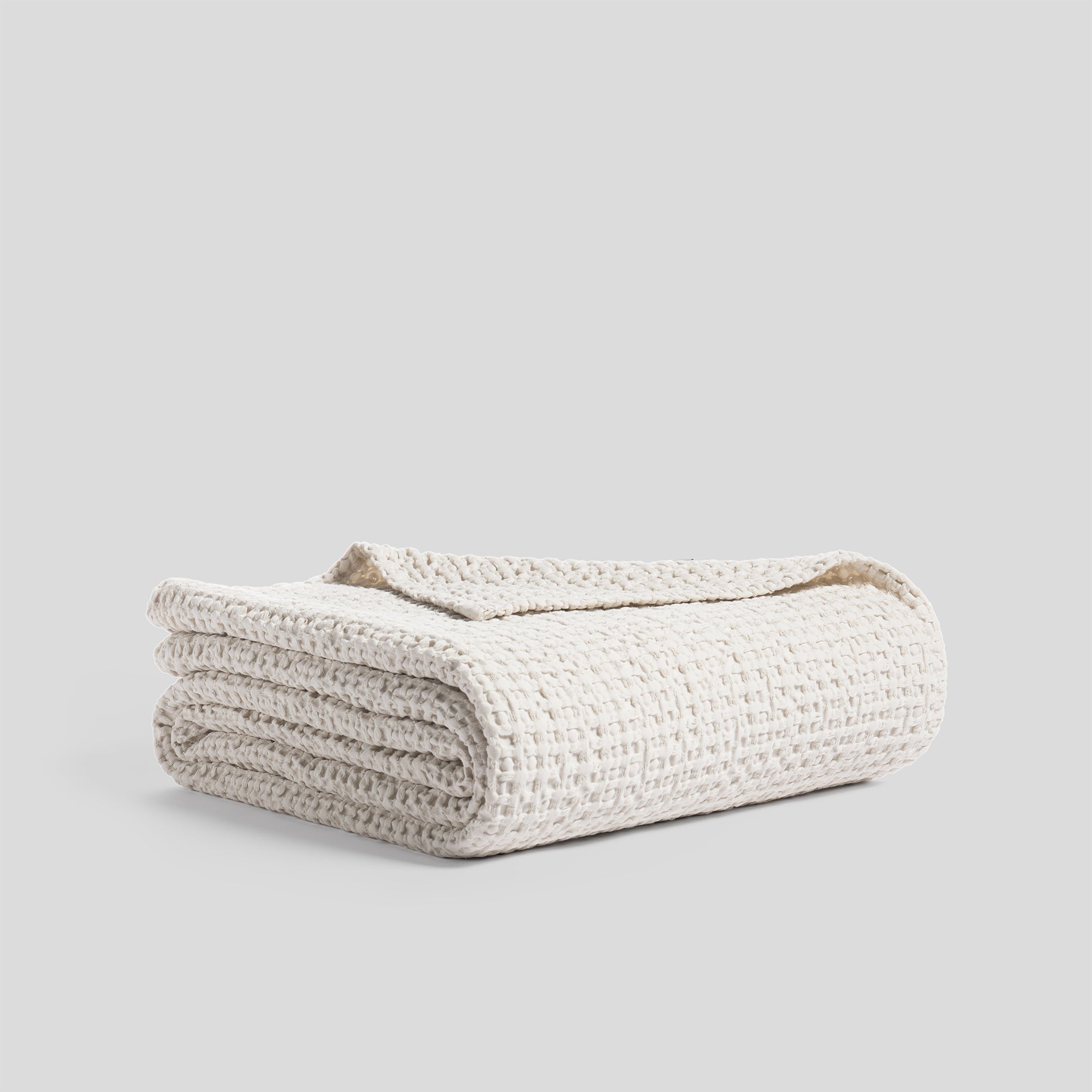 Folded bedspread made of heavy cotton with a waffle texture, in ivory color.