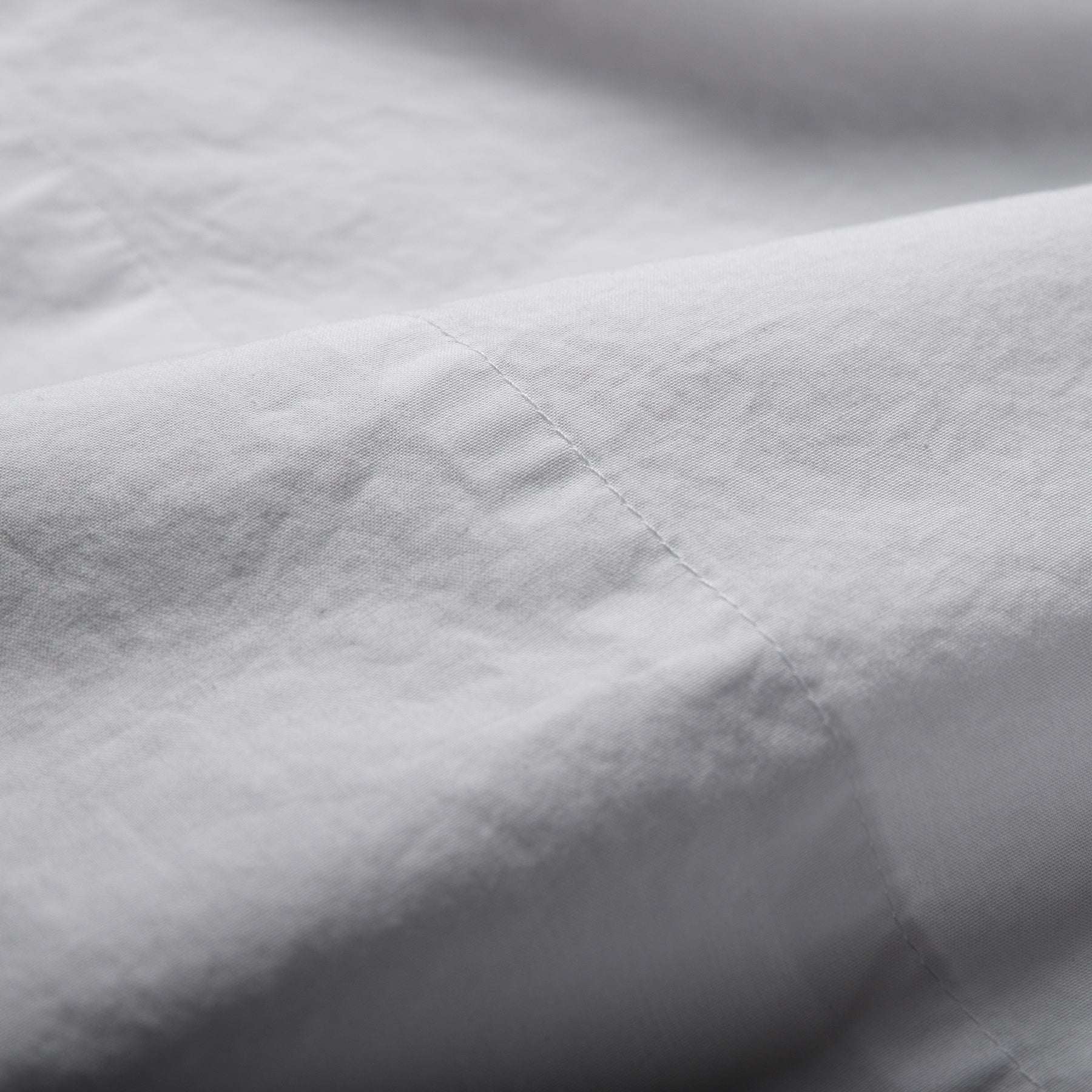 Close-up of pure white organic cotton flat sheet showing soft texture and stitched hemline.