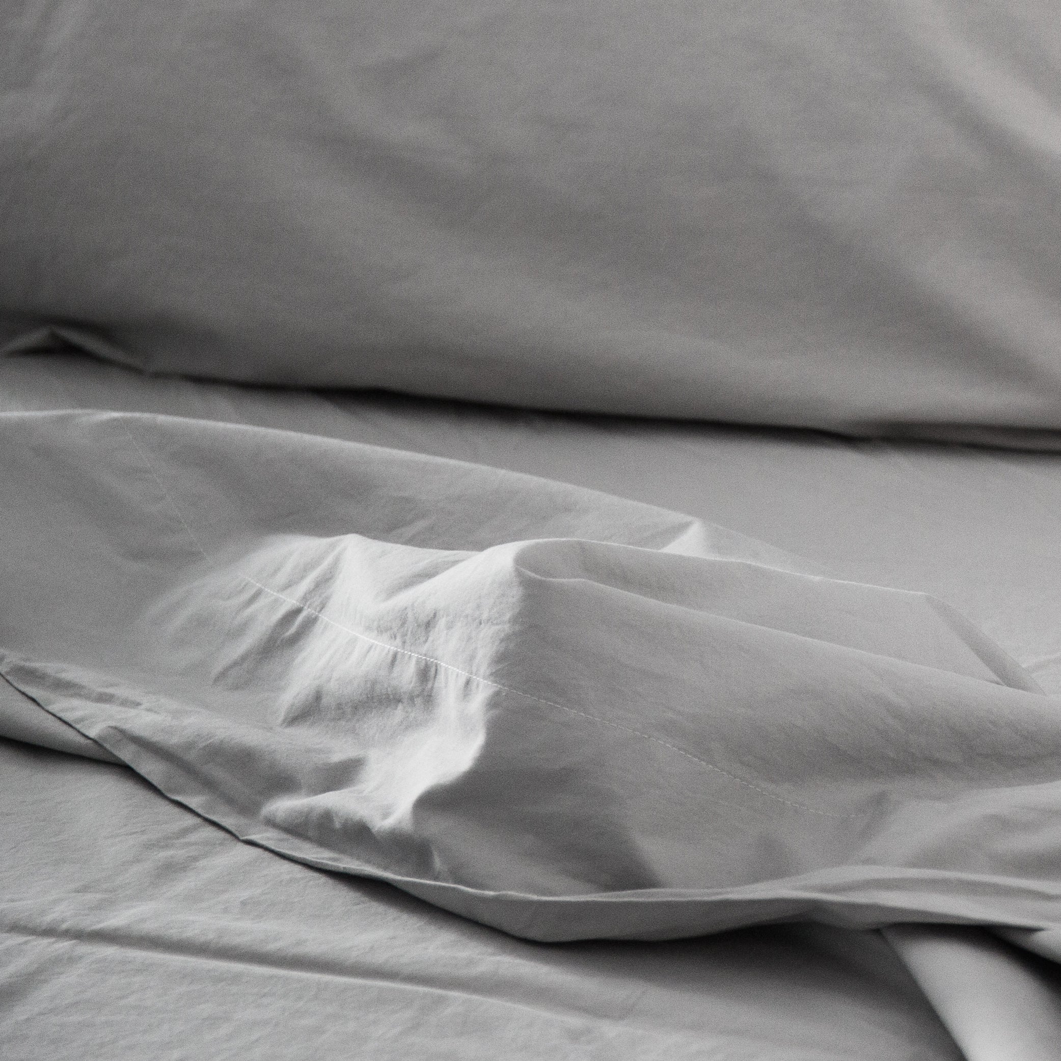 Flat sheet draped over a bed with soft folds and a smooth cotton finish.