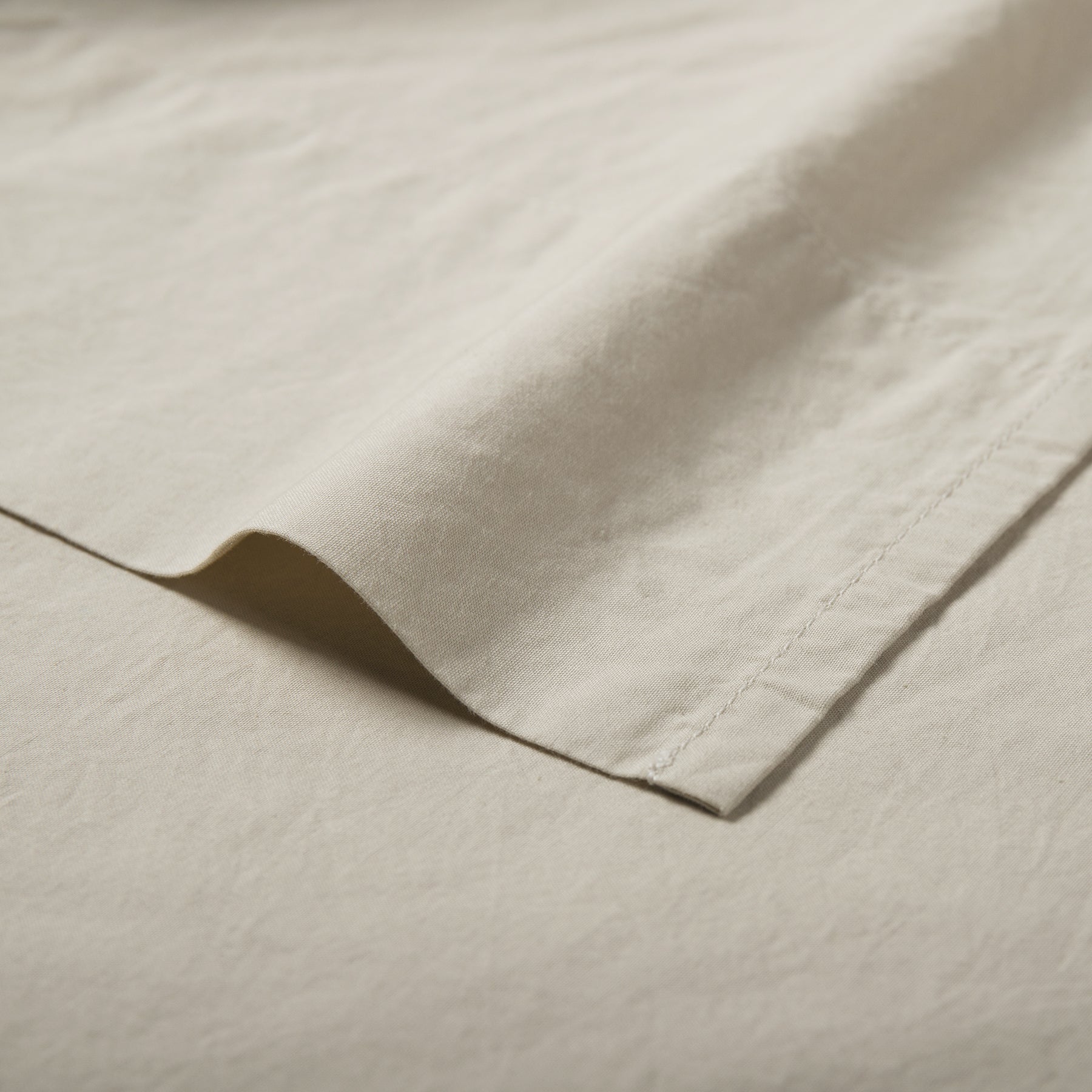 Close-up of sand organic cotton flat sheet showing soft texture and stitched hemline.