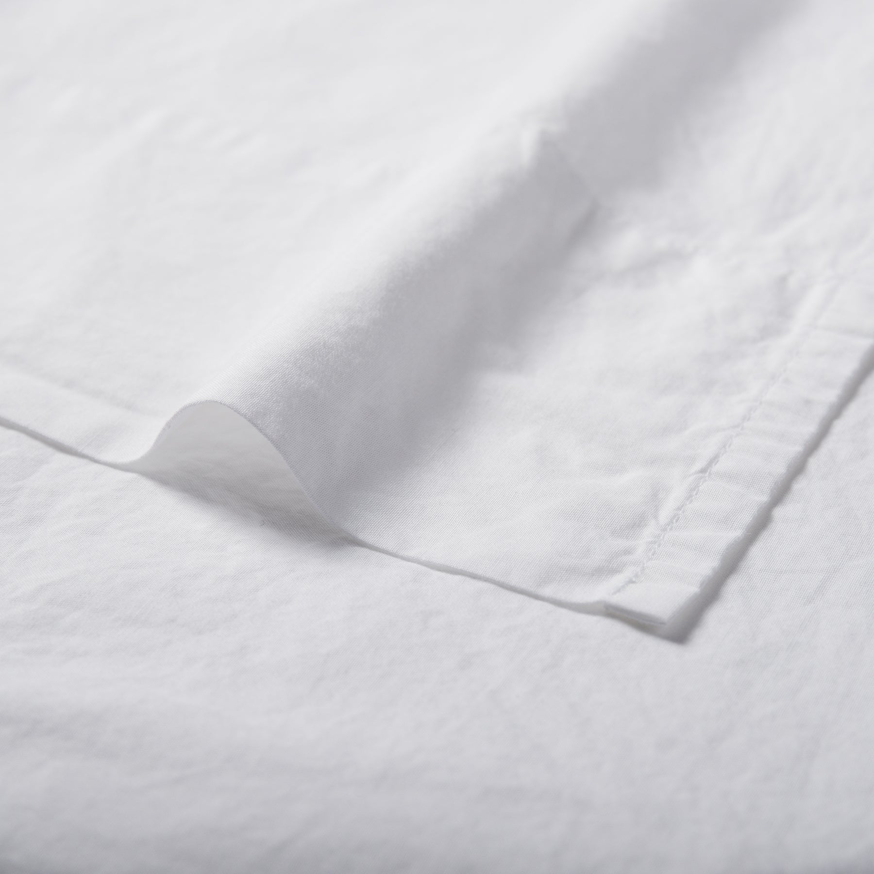 Close-up of pure white organic cotton flat sheet showing soft texture and stitched hemline.