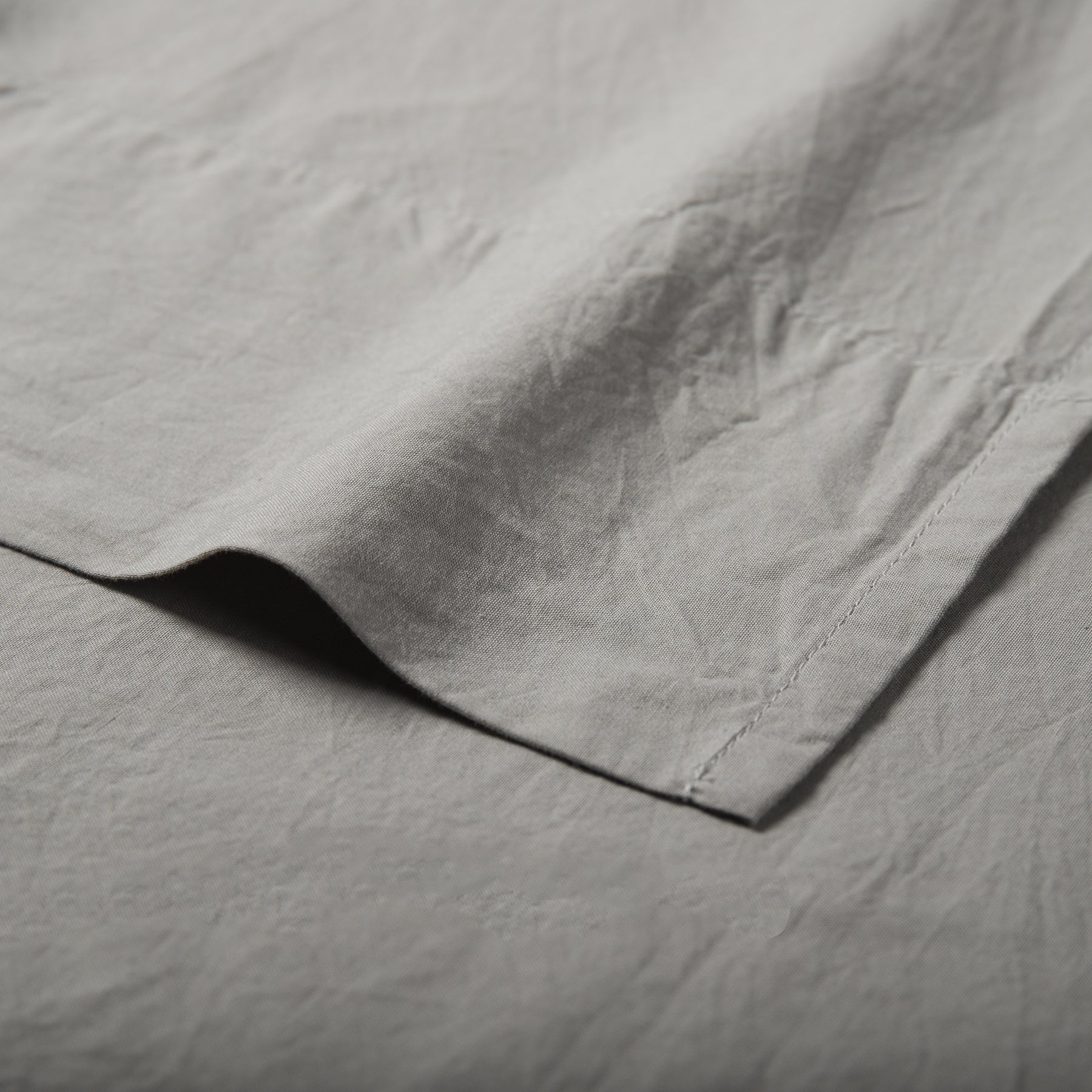 Close-up of mist grey organic cotton flat sheet showing soft texture and stitched hemline.
