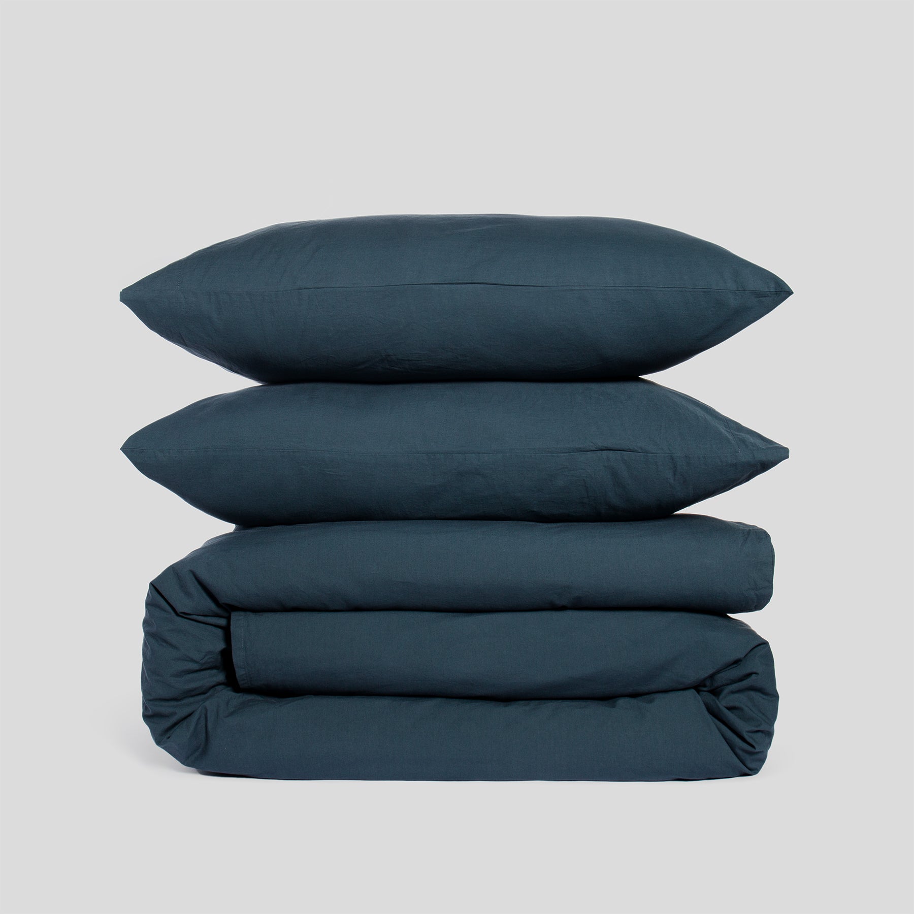 Duvet cover set in atlantic blue, including two stacked pillowcases and a folded duvet cover, made of organic cotton.
