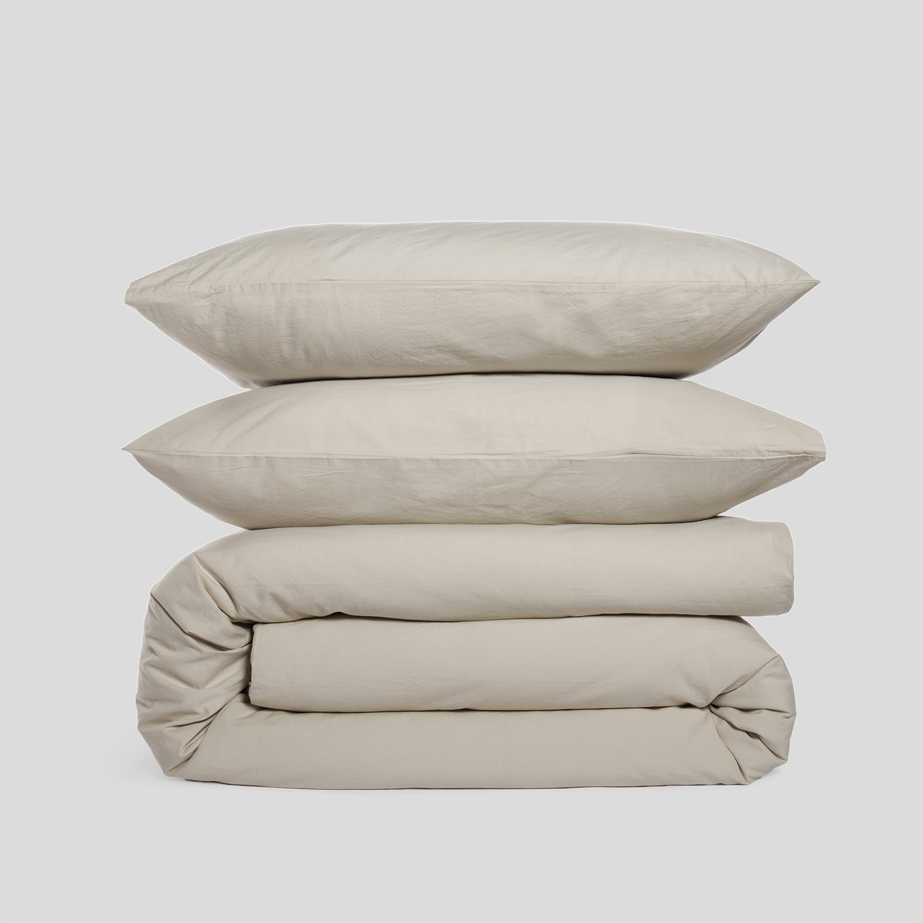 Duvet cover set in sand, including two stacked pillowcases and a folded duvet cover, made of organic cotton.