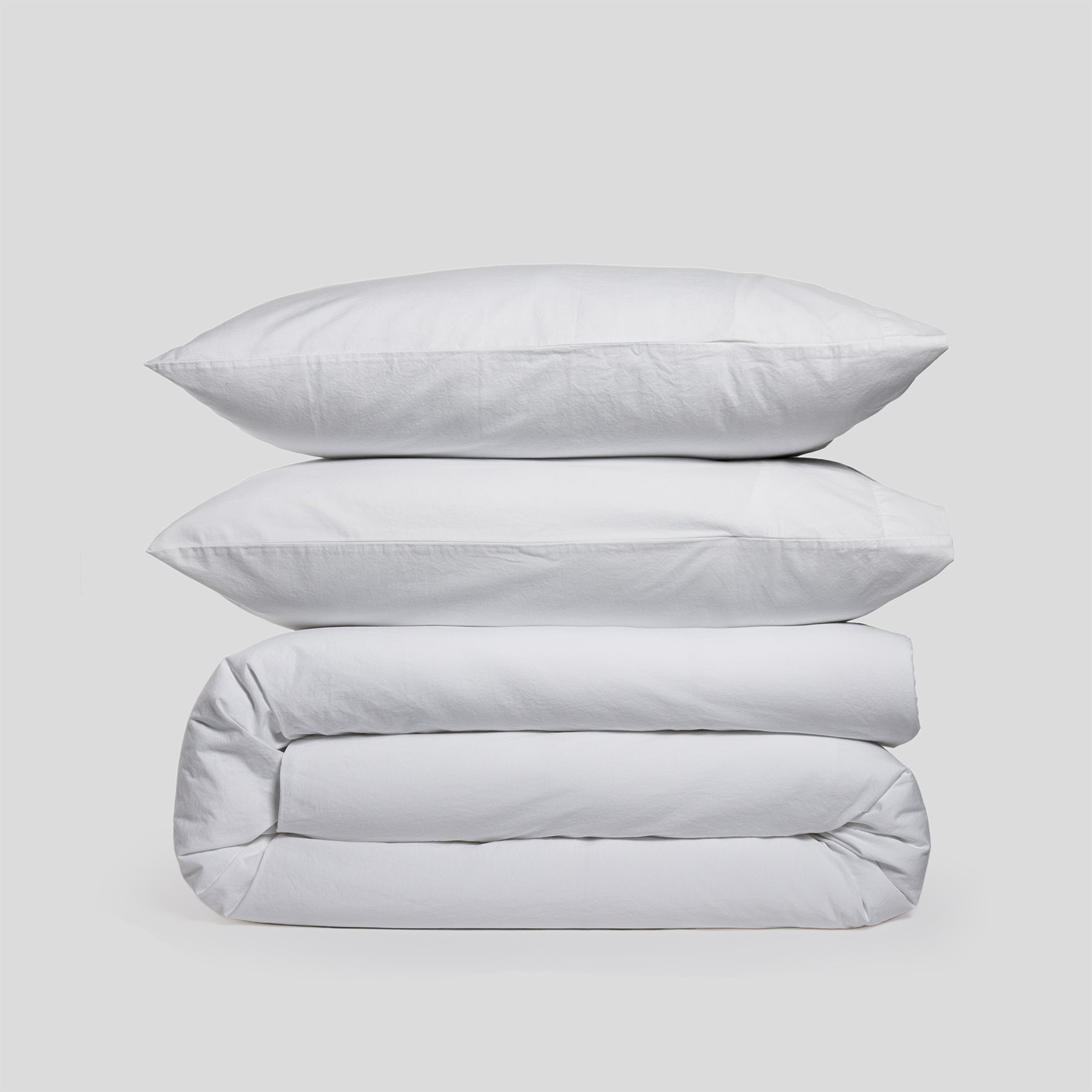 Duvet cover set in pure white, including two stacked pillowcases and a folded duvet cover, made of organic cotton.