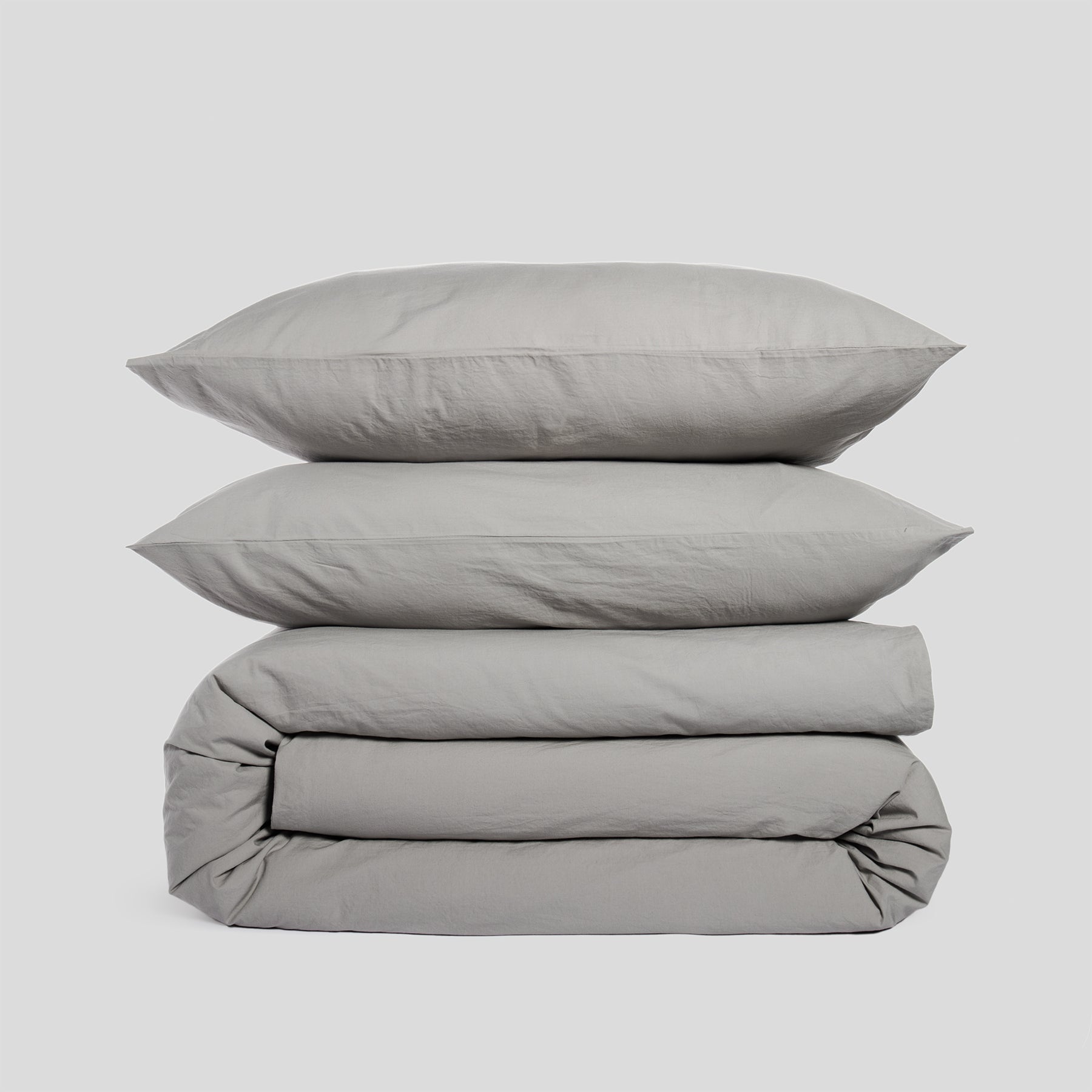 Duvet cover set in mist grey, including two stacked pillowcases and a folded duvet cover, made of organic cotton.