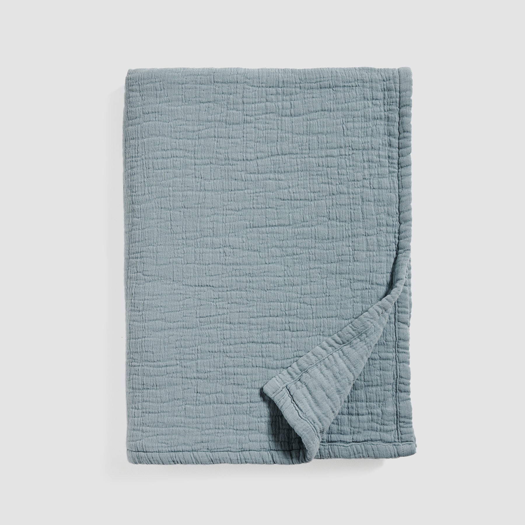 Folded soft cotton muslin blanket in slate blue color with a lightly textured surface.