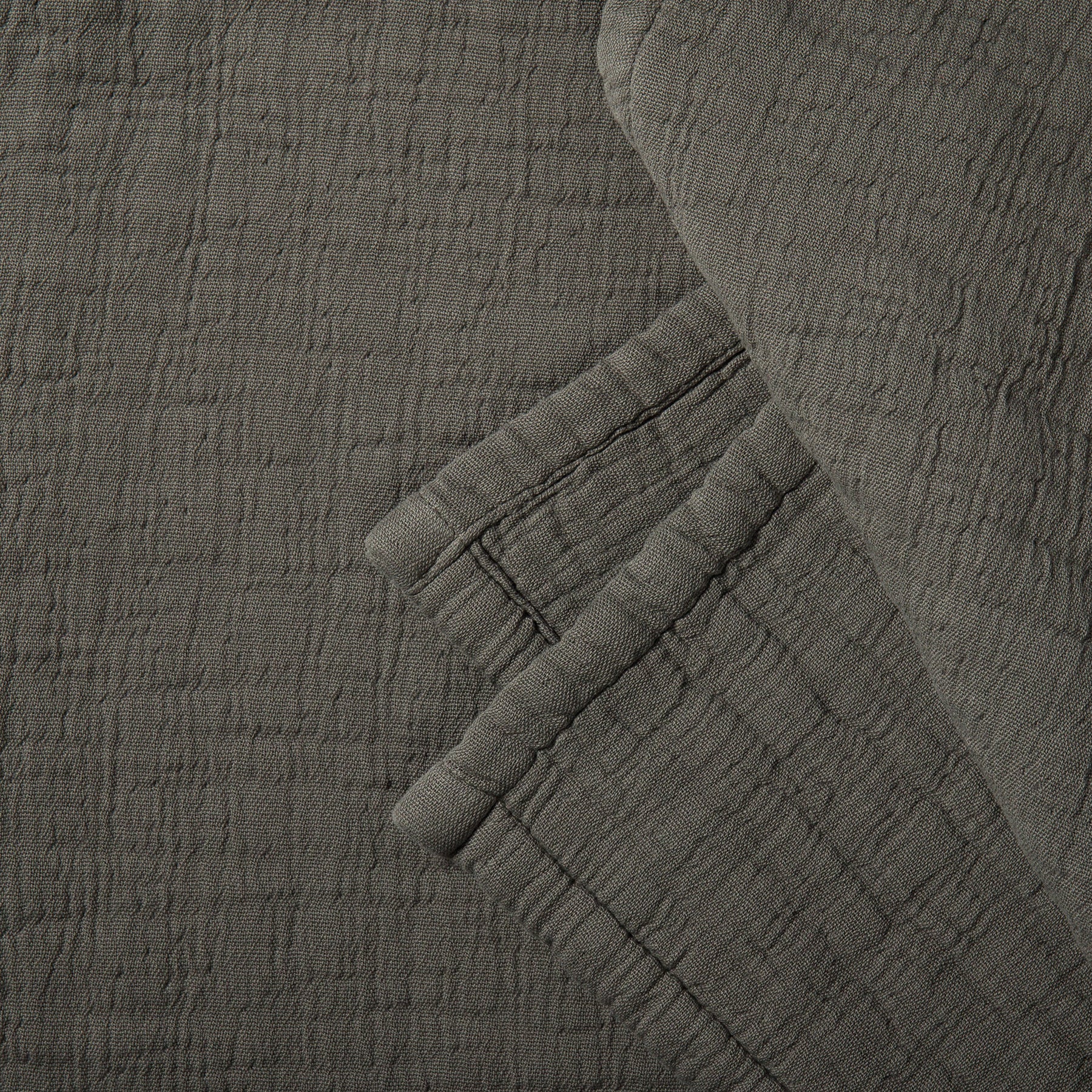 Close-up of a soft cotton muslin blanket in charcoal color showing a delicate crinkled texture.