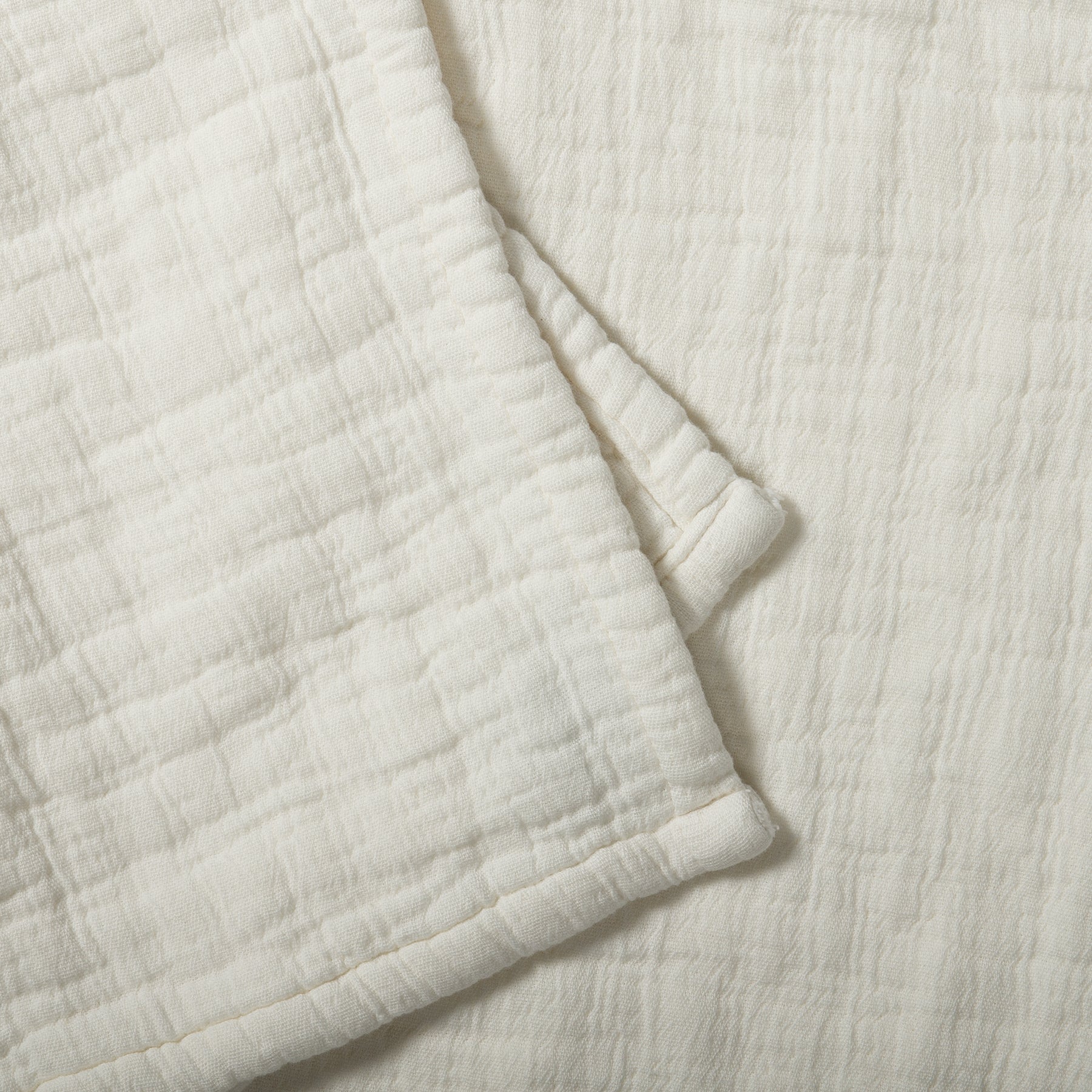 Close-up of a soft cotton muslin blanket in snow color showing a delicate crinkled texture.