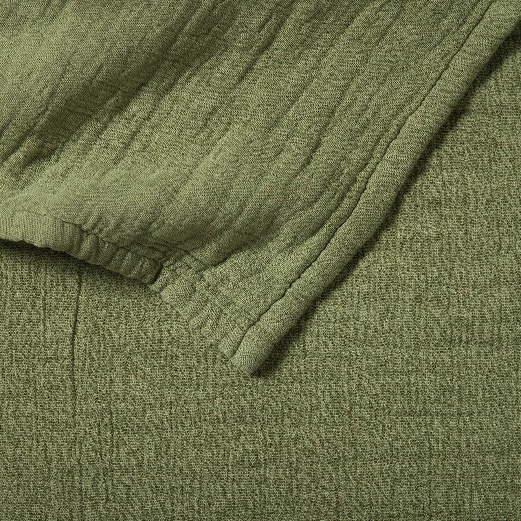 Close-up of a soft cotton muslin blanket in olive color showing a delicate crinkled texture.