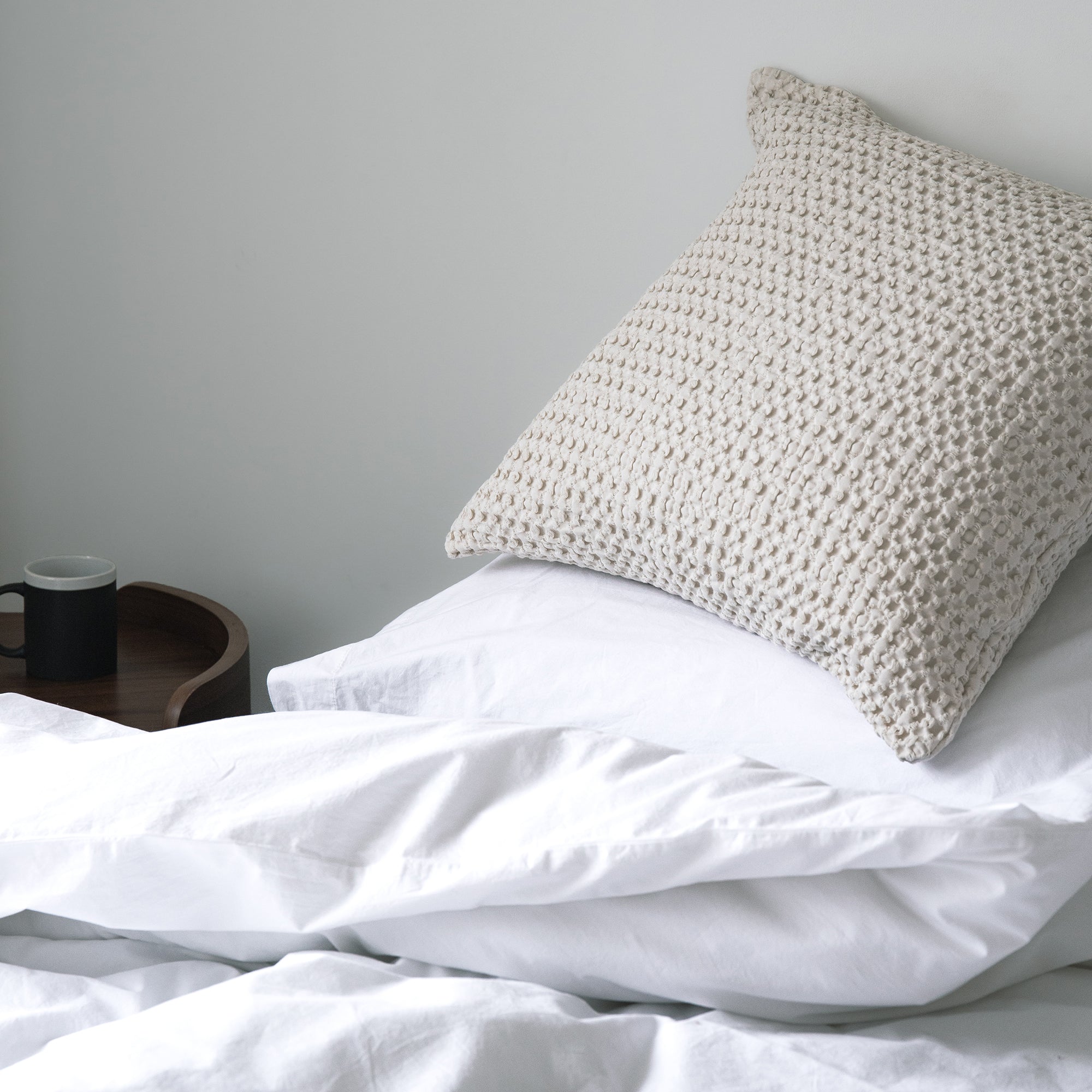 Waffle cushion cover styled on a bed with a textured and relaxed finish.