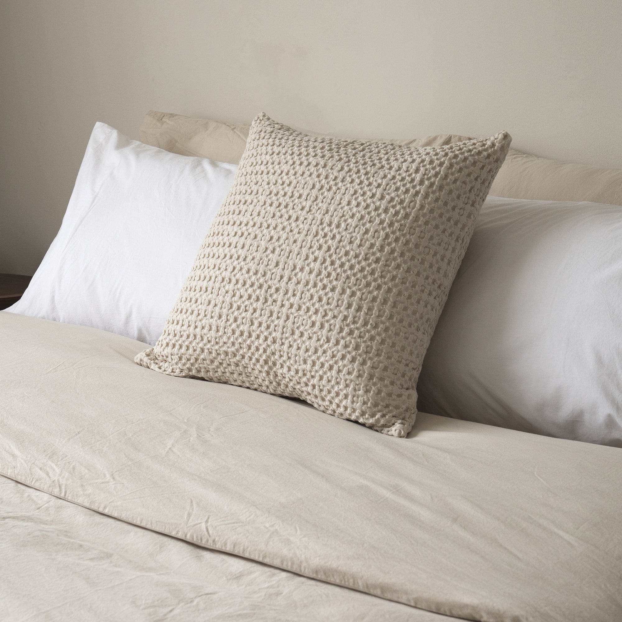 Textured waffle cushion cover layered with soft bedding for a cozy bedroom look.