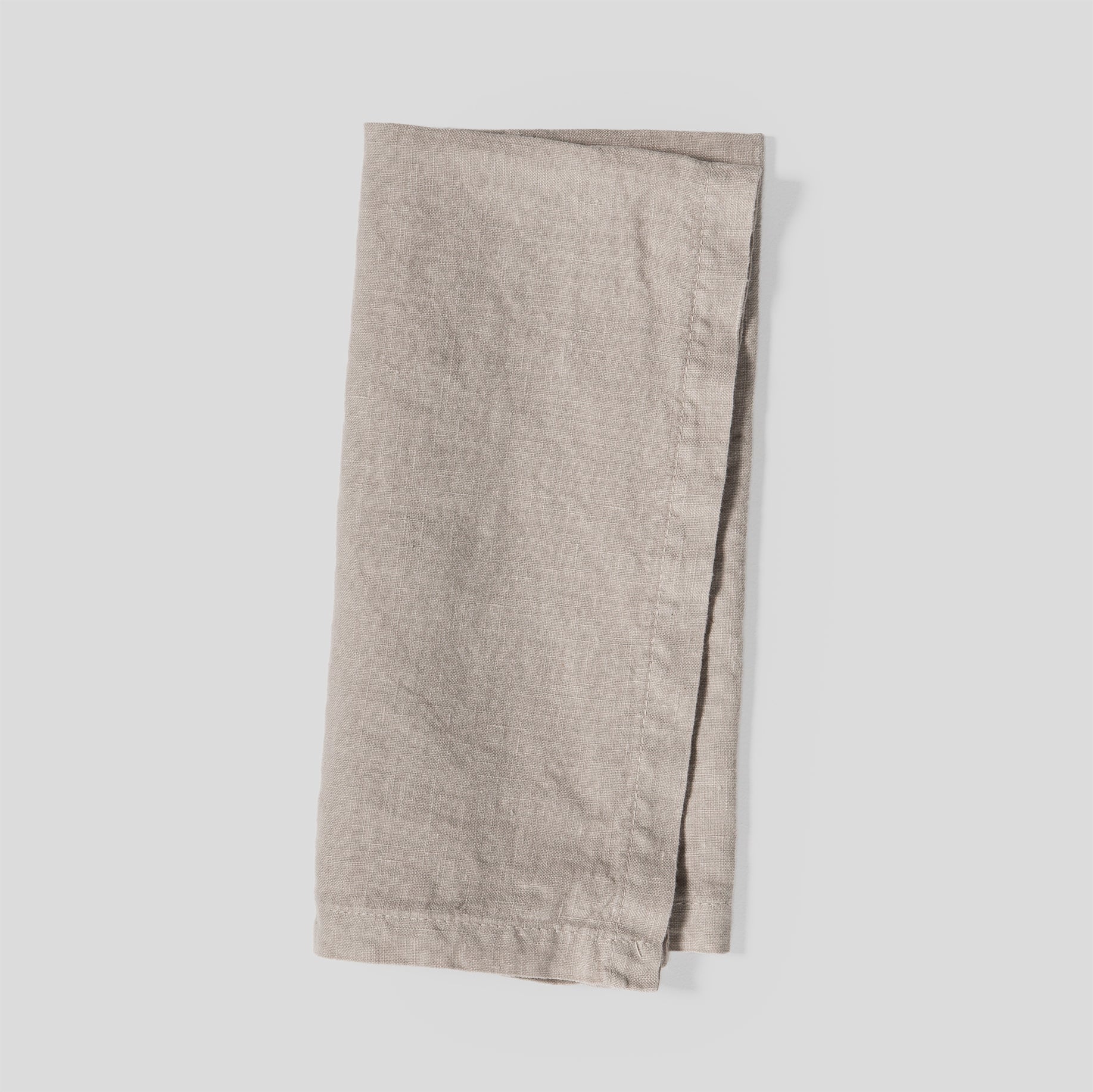 Folded light linen napkins in sand with a smooth, natural fabric texture.