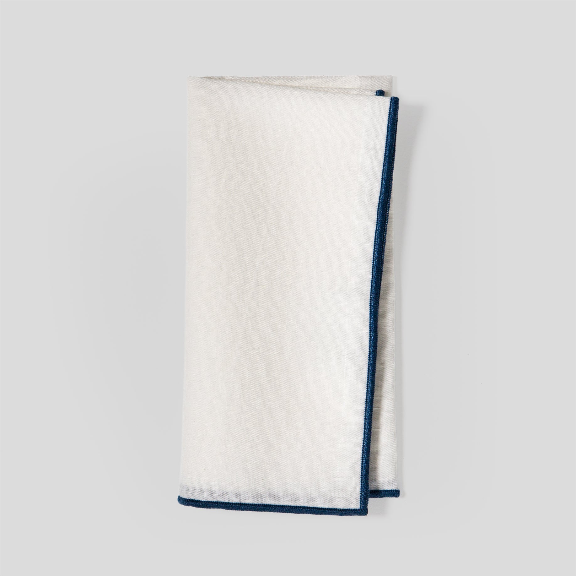 Folded linen and cotton napkins showing a natural fabric texture and indigo overlock edge detail.
