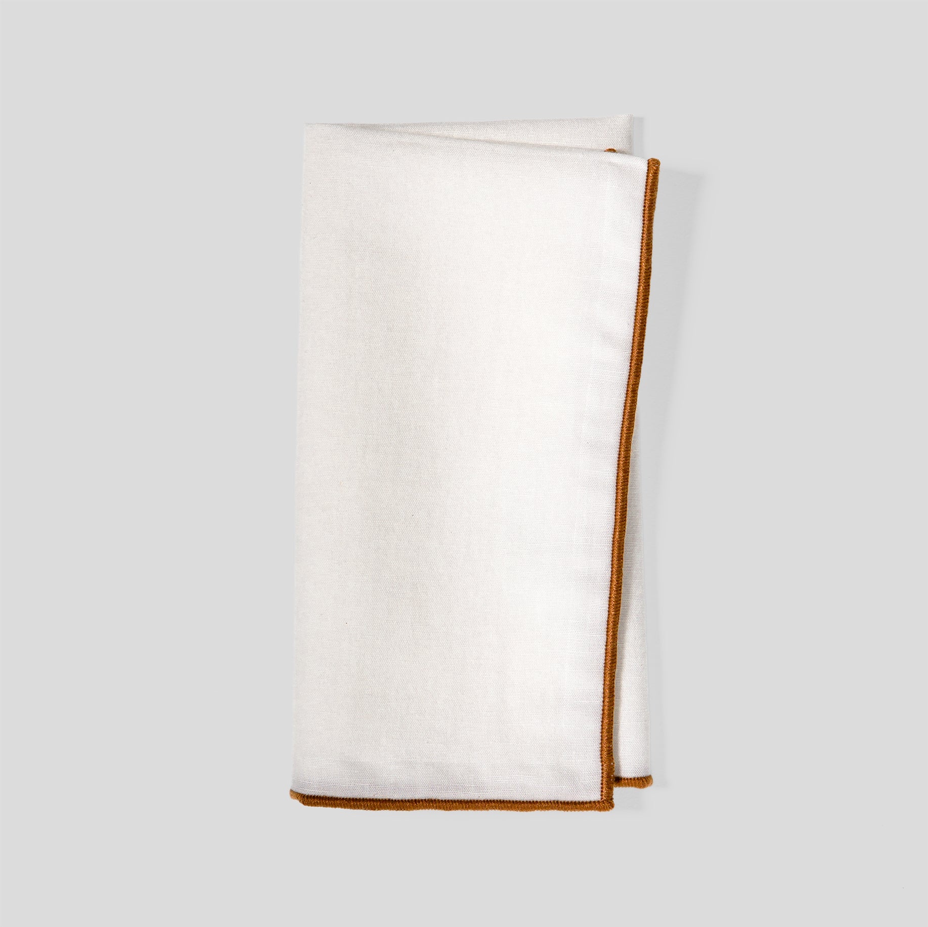 Folded linen and cotton napkins showing a natural fabric texture and amber clay overlock edge detail.