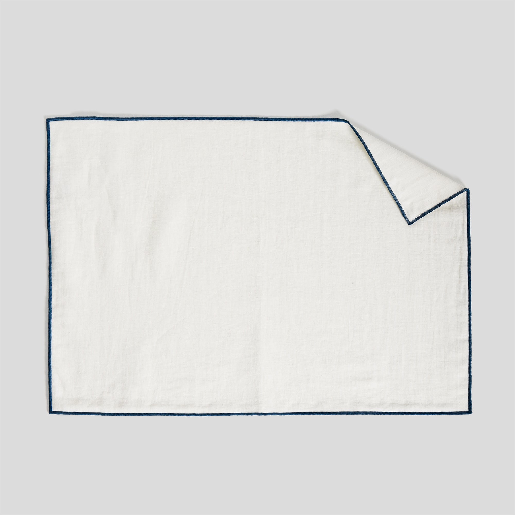 Linen and cotton placemat featuring a smooth surface and indigo overlock edge detail.