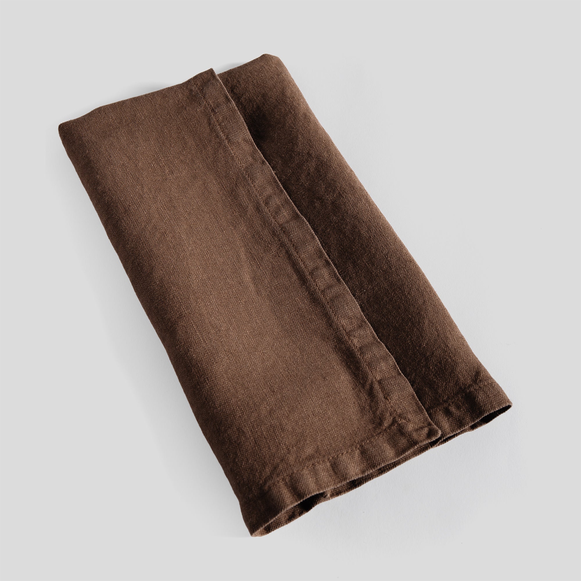 Folded sable linen napkin with refined stitching and a relaxed texture.
