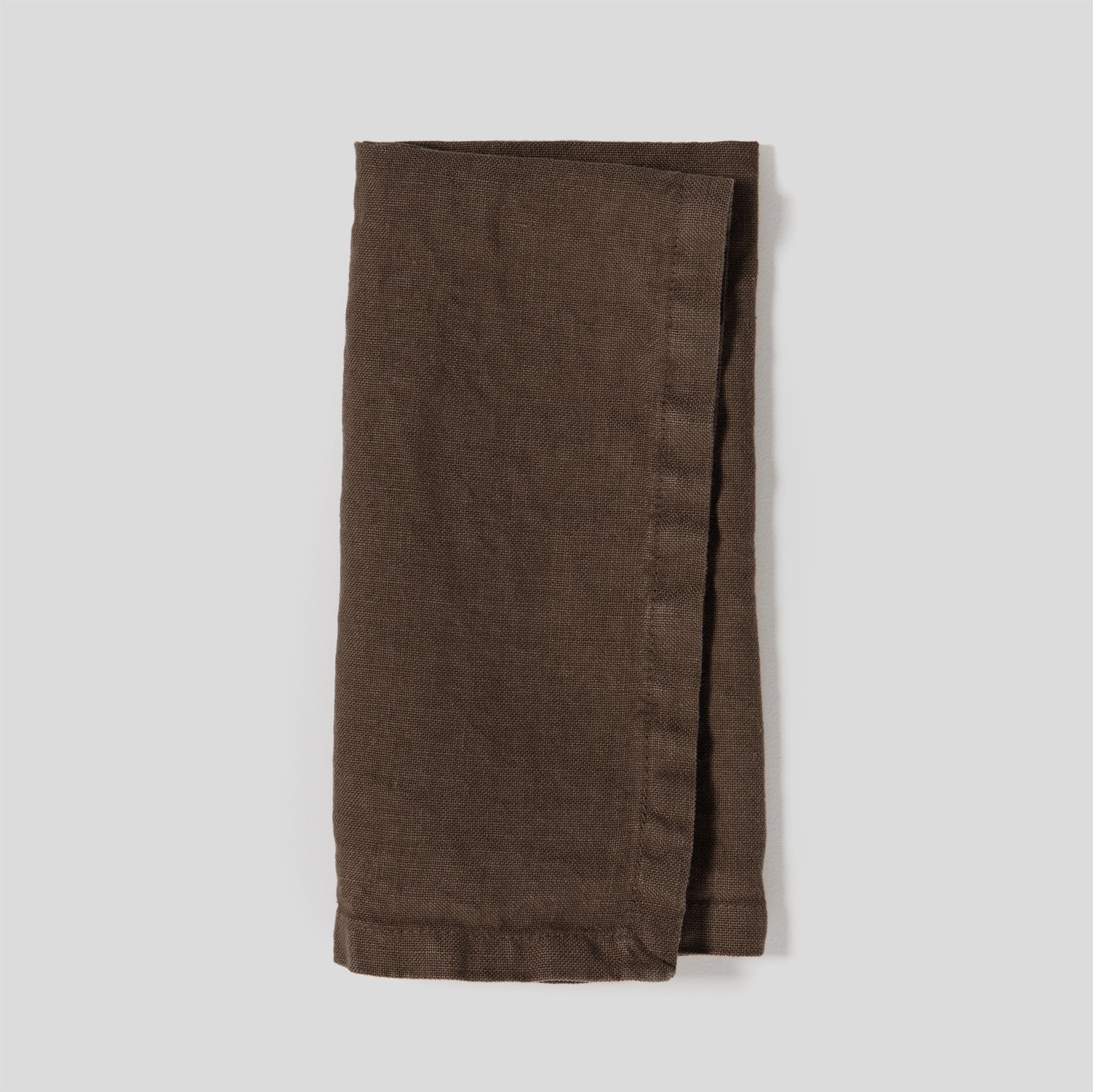 Folded heavy linen napkins in sable color with a dense, natural fabric texture.