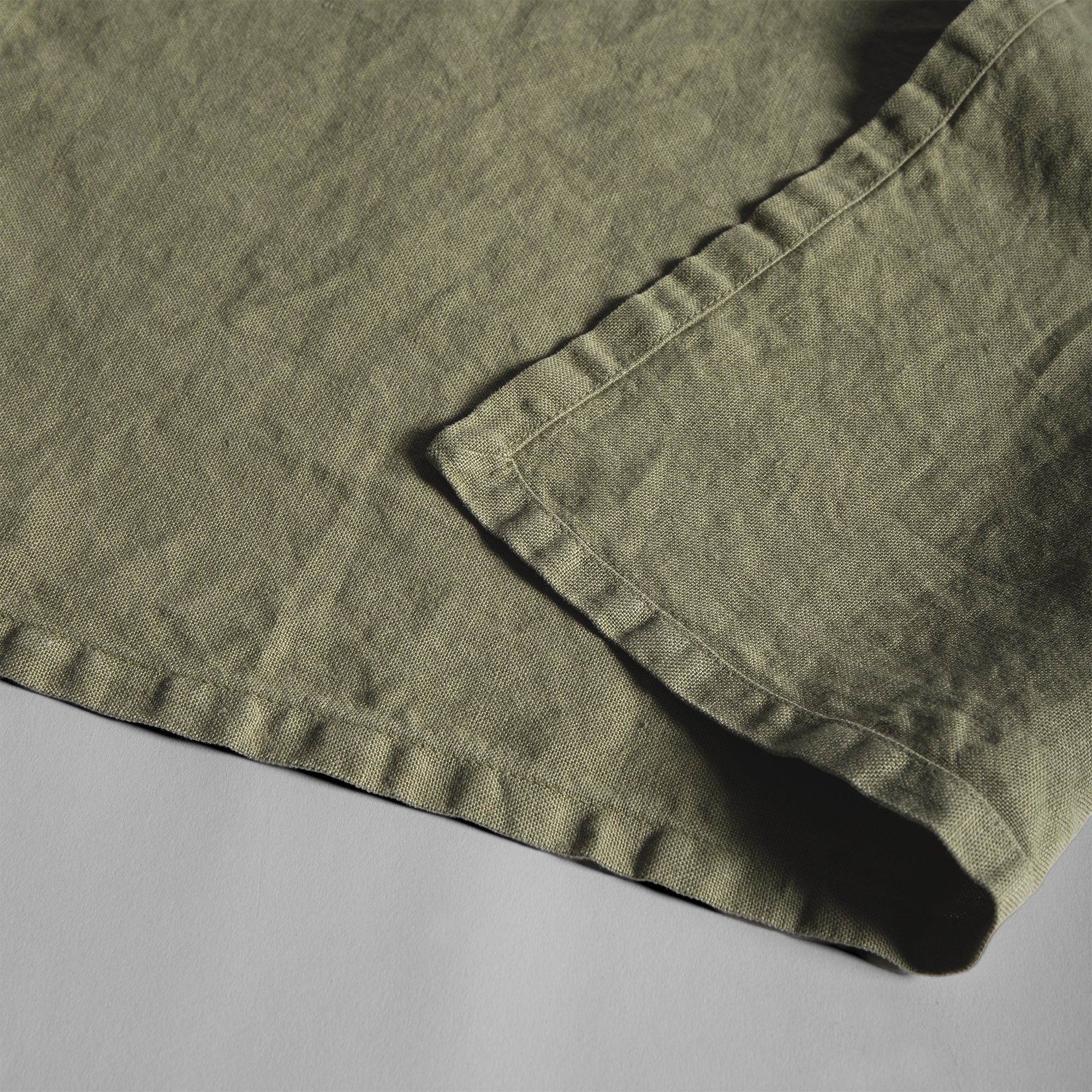 Olive linen placemat with soft texture and relaxed stitched edges.