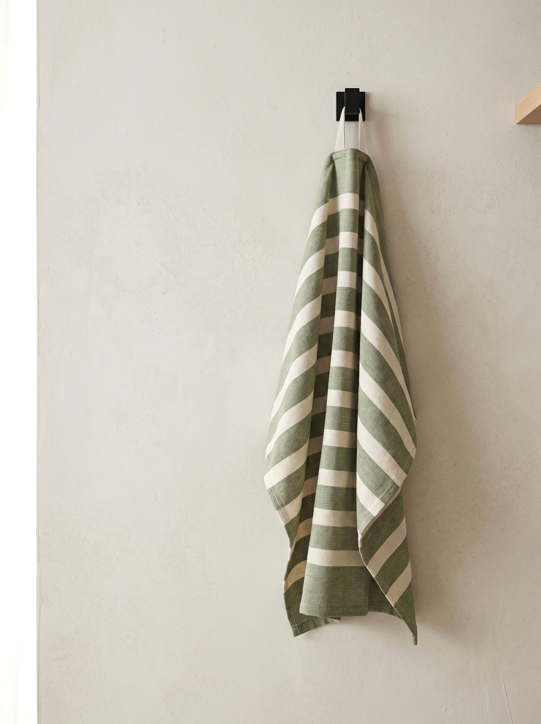 Olive striped 100% cotton kitchen towel hanging from a wall hook, bringing a relaxed and practical touch to the kitchen.